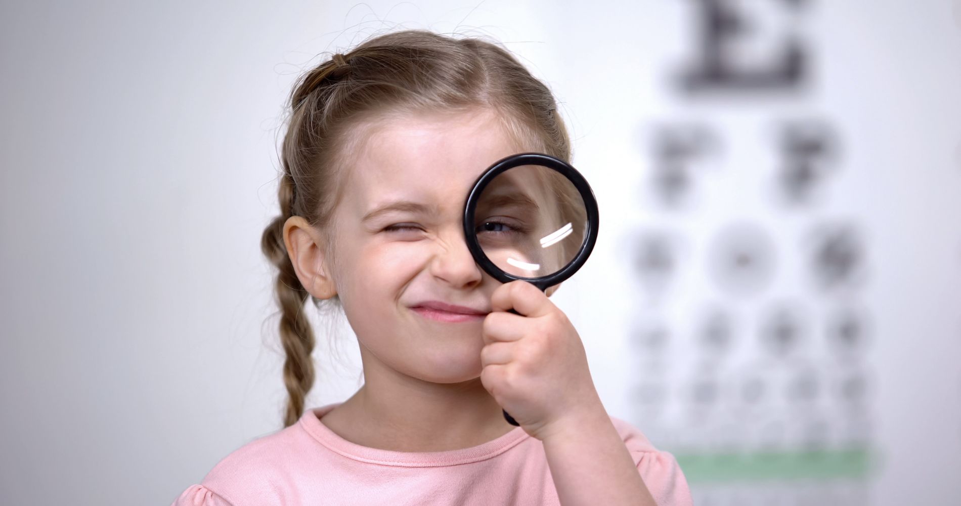 Dziewczynka z lupą przy oku podczas badania wzroku – symbol profilaktyki i dbania o zdrowe oczy.