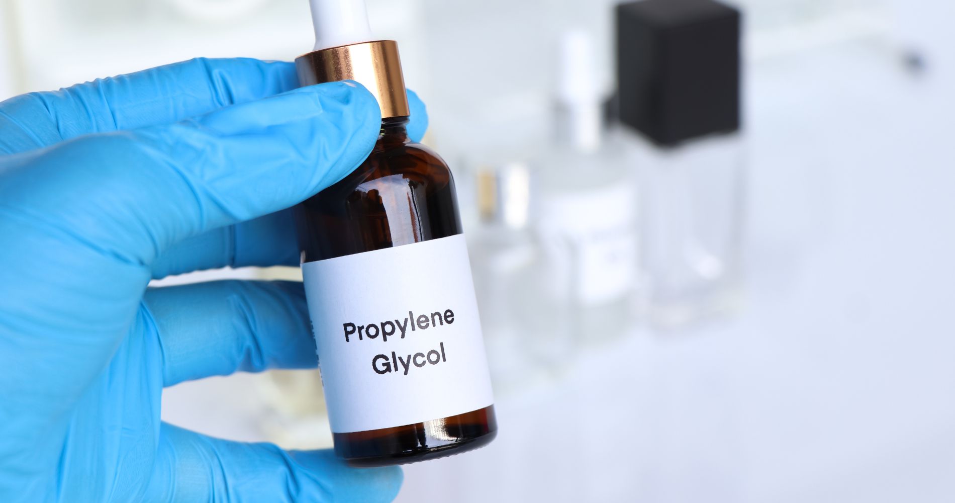 Butelka z glikolem propylenowym trzymana w rękawiczce laboratoryjnej – przykład składnika stosowanego w kosmetykach.