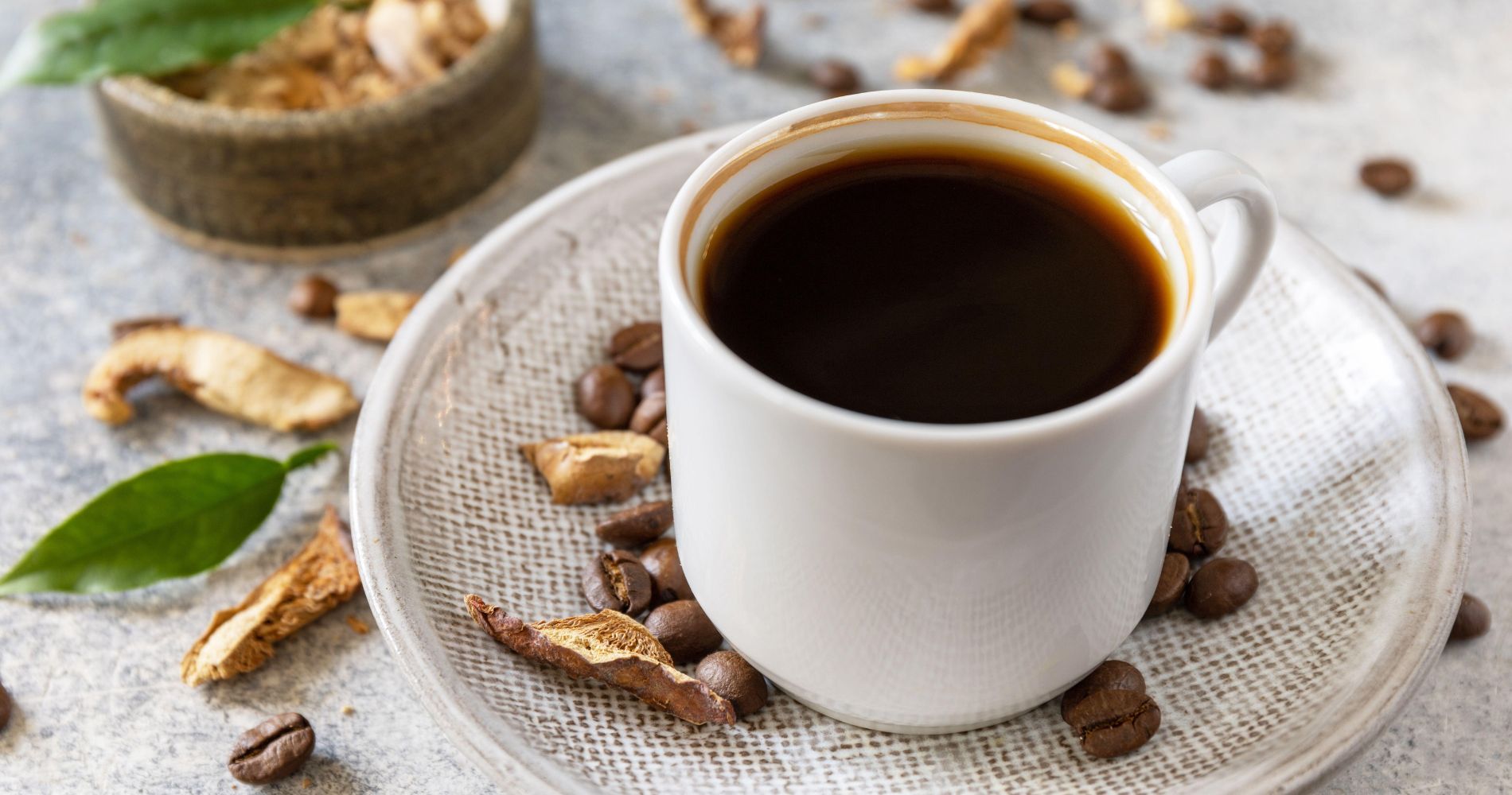 Filiżanka kawy z dodatkiem grzybów adaptogennych na talerzyku z ziarnami kawy.