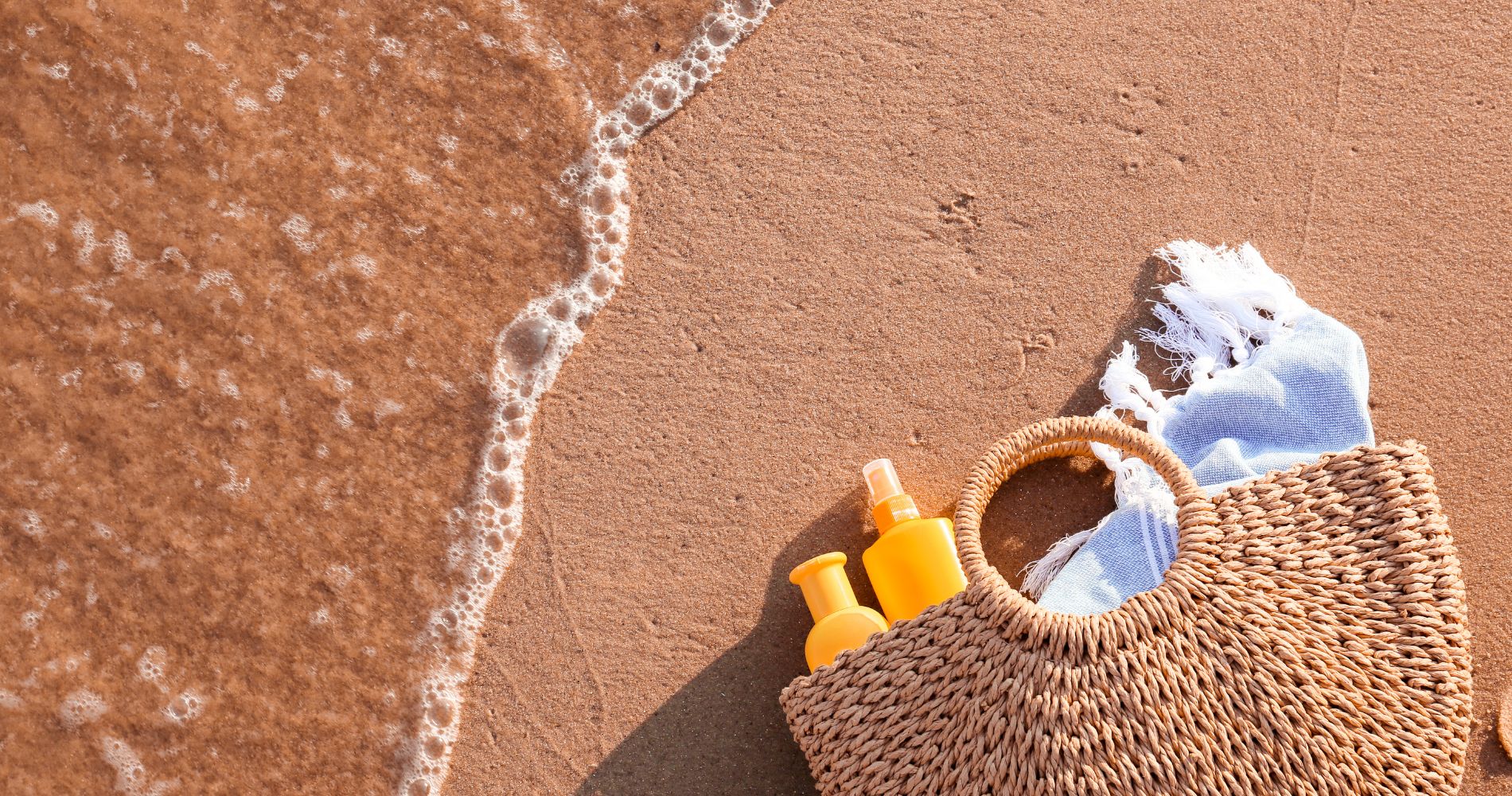 Kosmetyki przeciwsłoneczne w torbie plażowej na piasku.